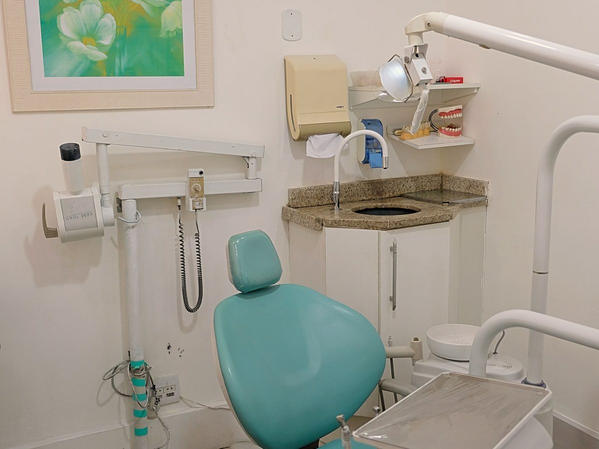 An empty dental room with a chair, daylight and neatly arranged equipment.
